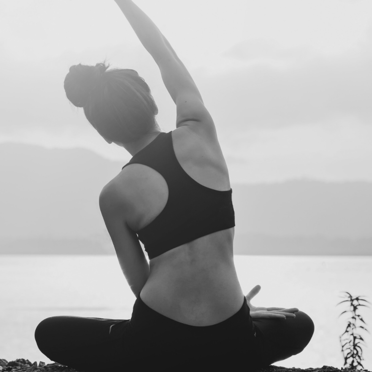 Frau in Sportbekleidung sitzt mit erhobenem Arm am Wasser, monochrom.