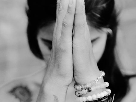 Eine Person mit gefalteten Händen in einem meditativen Pose, mit armbändern geschmückt.