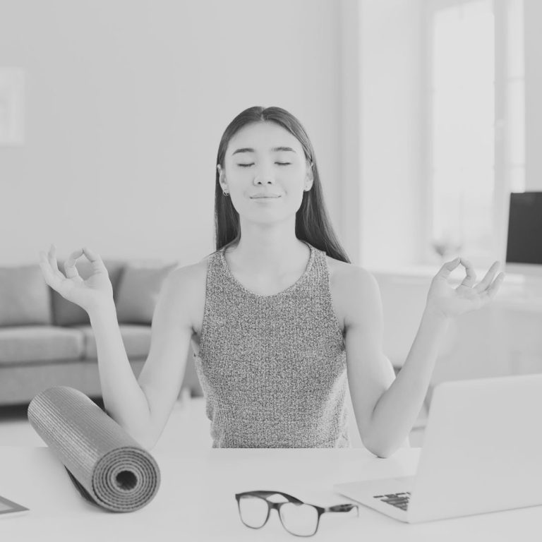 entspannt nach business yoga Junge Frau sitzt meditiert am Schreibtisch mit Laptop und Yogamatte.
